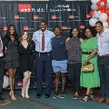 A group of individuals stands together at the Alpha Omega Alpha 2023 Induction Ceremony at UTMB, posing in front of a black logo backdrop with red and white balloon decorations to the sides.