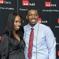 Two individuals pose together at the Alpha Omega Alpha 2023 Induction Ceremony at UTMB in front of a black UTMB Health and John Sealy School of Medicine logo backdrop, with red and white balloon decorations partially visible.