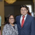 Two individuals stand together at the Alpha Omega Alpha 2023 Induction Ceremony at UTMB, posing in a softly lit indoor setting with neutral background elements visible behind them.