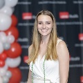 An individual poses at the Alpha Omega Alpha 2023 Induction Ceremony at UTMB, standing beside red and white balloon decorations with a black logo backdrop behind.
