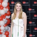 An individual poses alone at the Alpha Omega Alpha 2023 Induction Ceremony at UTMB, standing near red and white balloon decorations and a black logo backdrop.