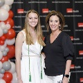 Two individuals pose together at the Alpha Omega Alpha 2023 Induction Ceremony at UTMB, standing in front of a black step-and-repeat backdrop with red and white balloon decorations visible to the side.