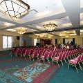 Banquet room with rows of chairs facing a stage area, illuminated ceiling fixtures, and UTMB 2024 event decorations for an Alpha Omega Alpha Texas Alpha Chapter ceremony.