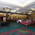 Audience seated in rows facing a stage and podium in a banquet room with UTMB event backdrop and decorations during an Alpha Omega Alpha Texas Alpha Chapter ceremony.