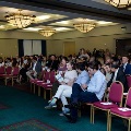 Audience seated in rows of red chairs in a banquet room, facing a stage area during an Alpha Omega Alpha Texas Alpha Chapter ceremony at UTMB.