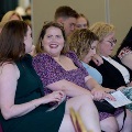 Row of attendees seated in red chairs, conversing and holding event programs during an Alpha Omega Alpha Texas Alpha Chapter ceremony at UTMB.