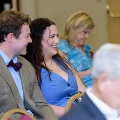 Two attendees sit in red chairs smiling and looking toward each other during an Alpha Omega Alpha Texas Alpha Chapter event at UTMB, with other audience members seated behind them.