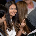 Seated attendee gestures with one finger while holding a program and conversing with neighbors during an Alpha Omega Alpha Texas Alpha Chapter event at UTMB.