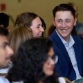 Two attendees seated among a larger audience turn toward each other while holding programs during an Alpha Omega Alpha Texas Alpha Chapter event at UTMB.