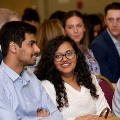 Two attendees seated in a row of red chairs converse, with one holding a program, during an Alpha Omega Alpha Texas Alpha Chapter event at UTMB.