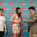Individual presents a green honor cord to another attendee in front of a UTMB Health backdrop, with a third attendee standing nearby during an Alpha Omega Alpha Texas Alpha Chapter event.