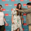 Presenter places green honor cords on an attendee wearing a floral dress in front of a UTMB Health backdrop, with another attendee observing during an Alpha Omega Alpha Texas Alpha Chapter ceremony.