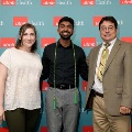 Three individuals stand together in front of a UTMB Health backdrop, with one wearing green honor cords, during an Alpha Omega Alpha Texas Alpha Chapter recognition event.