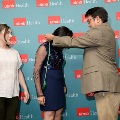 Presenter places green honor cords on an attendee wearing a navy dress in front of a UTMB Health backdrop, with another attendee observing during an Alpha Omega Alpha Texas Alpha Chapter ceremony.