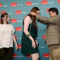 Presenter places green honor cords on an attendee in a dark green dress in front of a UTMB Health backdrop, with another attendee observing during an Alpha Omega Alpha Texas Alpha Chapter ceremony.