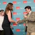 Two individuals shake hands while one holds green honor cords in front of a UTMB Health backdrop, with another attendee nearby during an Alpha Omega Alpha Texas Alpha Chapter ceremony.