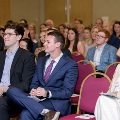 Audience seated in rows of red chairs, including attendees in formal attire holding programs during an Alpha Omega Alpha Texas Alpha Chapter ceremony at UTMB.