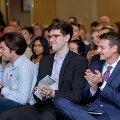 Front-row attendees seated in red chairs clap while holding programs during an Alpha Omega Alpha Texas Alpha Chapter ceremony at UTMB.