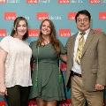 Three individuals stand together in front of a UTMB Health backdrop, with one wearing green honor cords, during an Alpha Omega Alpha Texas Alpha Chapter recognition event.