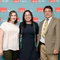 Three individuals pose indoors in front of a UTMB Health and John Sealy School of Medicine branded backdrop with repeating red logo panels, dressed in semi-formal attire and standing close together.