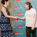 Individual in a dark patterned dress shakes hands with another individual near a small stage, with a UTMB Health branded backdrop and podium visible nearby in a softly lit indoor ceremony setting.