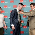 Individual in a blue suit leans forward as another individual places green honor cords around the neck in front of a UTMB Health and John Sealy School of Medicine branded backdrop, with a third person standing nearby.