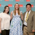 Three individuals pose indoors in front of a UTMB Health and John Sealy School of Medicine branded backdrop with repeating logos, dressed in semi-formal attire and standing close together for a photo.