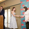 Individual in a patterned sleeveless dress shakes hands with another individual near a small stage, with a UTMB Health branded backdrop, podium, and curtain visible in a softly lit indoor ceremony setting.