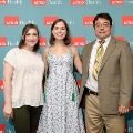 Three individuals pose indoors in front of a UTMB Health and John Sealy School of Medicine branded backdrop with repeating red logo panels, dressed in semi-formal attire and standing close together.