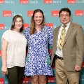 Three individuals pose indoors in front of a UTMB Health and John Sealy School of Medicine branded backdrop with repeating logos, dressed in semi-formal attire and standing close together for a photo.