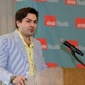 Individual stands at a wooden podium speaking into a microphone, with a UTMB Health branded backdrop behind and notes placed on the podium in a softly lit indoor ceremony setting.