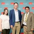 Three individuals pose indoors in front of a UTMB Health and John Sealy School of Medicine branded backdrop featuring repeating red and white logos, dressed in semi-formal attire and standing close together.