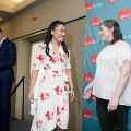 Individual in a white floral dress stands near a small stage shaking hands with another individual in front of a UTMB Health branded backdrop, with a podium and microphone visible to the side.