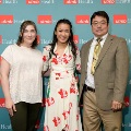Three individuals pose indoors in front of a UTMB Health and John Sealy School of Medicine branded backdrop with repeating logos, dressed in semi-formal attire and standing close together for a photo.