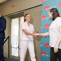 Individual in a light-colored outfit shakes hands with another individual near a small stage, with a UTMB Health branded backdrop and a podium visible nearby in a softly lit indoor ceremony setting.