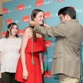 One individual places green honor cords over another individual’s shoulders in front of a UTMB Health branded backdrop, while a third person stands nearby in semi-formal attire.
