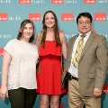 Three individuals pose indoors in front of a UTMB Health and John Sealy School of Medicine branded backdrop, with repeating logos, dressed in semi-formal attire and standing close together.