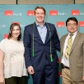Three individuals pose indoors in front of a UTMB Health and John Sealy School of Medicine branded backdrop, with one wearing green honor cords, all dressed in semi-formal attire and standing close together.