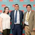 Three individuals pose indoors in front of a UTMB Health and John Sealy School of Medicine branded backdrop, all in semi-formal attire, standing close together for a group photo.