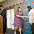 Two individuals shake hands on a small stage near a podium in front of a UTMB Health branded backdrop, while another individual stands at the podium, in a formal indoor ceremony setting with event lighting overhead.