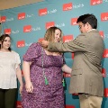 Individual places green honor cords over another individual’s head in front of a UTMB Health branded backdrop, with a second person waiting nearby, all dressed in semi-formal attire in an indoor ceremony setting.
