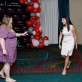 Two individuals approach each other and gesture in greeting in front of a UTMB Health and John Sealy School of Medicine branded backdrop with red, white, and gray balloon arch, in an indoor event space with chairs nearby.