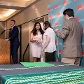 Individuals stand on a small stage near a podium during a ceremony as one prepares to place green honor cords on another, with a UTMB Health branded backdrop behind and tables with cords visible in the foreground.