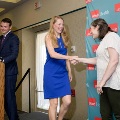 Two individuals shake hands on a small stage near a podium in front of a UTMB Health branded backdrop, with one wearing green honor cords and another person standing at the podium in a formal indoor ceremony setting.