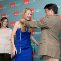 Individual in a blue dress stands as another person places green honor cords around the neck in front of a UTMB Health branded backdrop, with a third individual nearby in a semi-formal indoor ceremony setting.