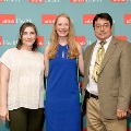 Three individuals pose indoors in front of a UTMB Health and John Sealy School of Medicine branded backdrop, with red and white logo panels, one wearing green honor cords, all dressed in semi-formal attire.