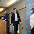 Individual in a suit walks toward a podium on a small stage where another person stands, with a UTMB Health branded backdrop to the side and event lighting overhead in an indoor ceremony setting.