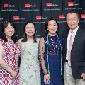 Four individuals pose indoors in front of a UTMB Health and John Sealy School of Medicine branded backdrop, framed by red, white, and gray balloon decorations, with one wearing green honor cords and all in semi-formal attire.