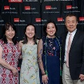 Four individuals pose indoors in front of a UTMB Health and John Sealy School of Medicine branded backdrop, framed by red, white, and gray balloon decorations, with one wearing green honor cords and all in semi-formal attire.