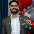 Individual in a suit stands indoors holding green honor cords in front of a UTMB Health and John Sealy School of Medicine branded backdrop, with red, white, and gray balloon decorations visible to the side.